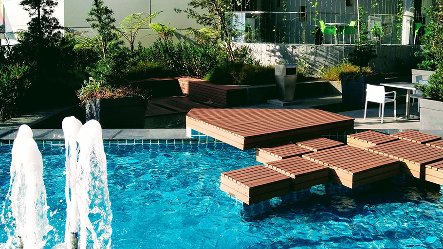 A wooden deck built out over a portion of a swimming pool with a fountain