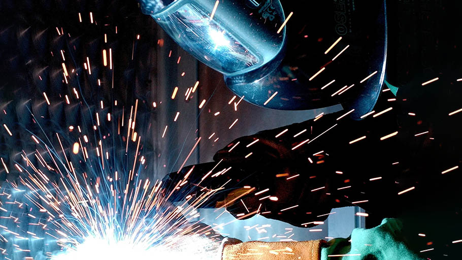 A welder wearing a welding mask is joining steel