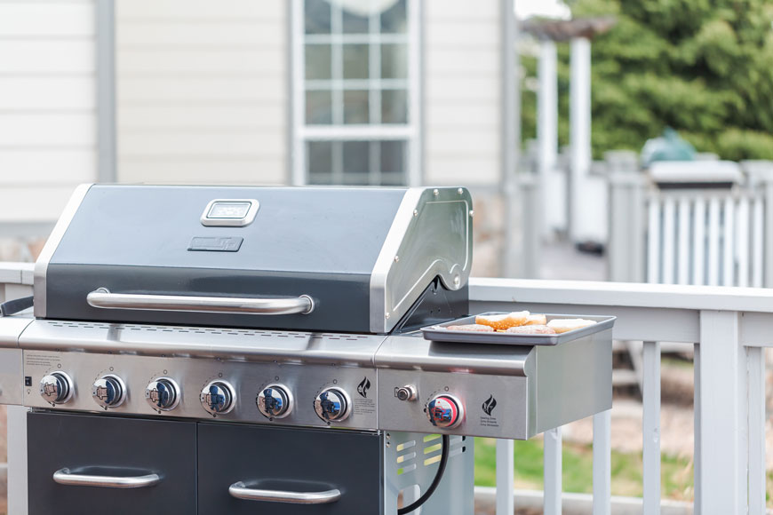 A BBQ on a backyard patio with a black enameled lid and shiny stainless steel components