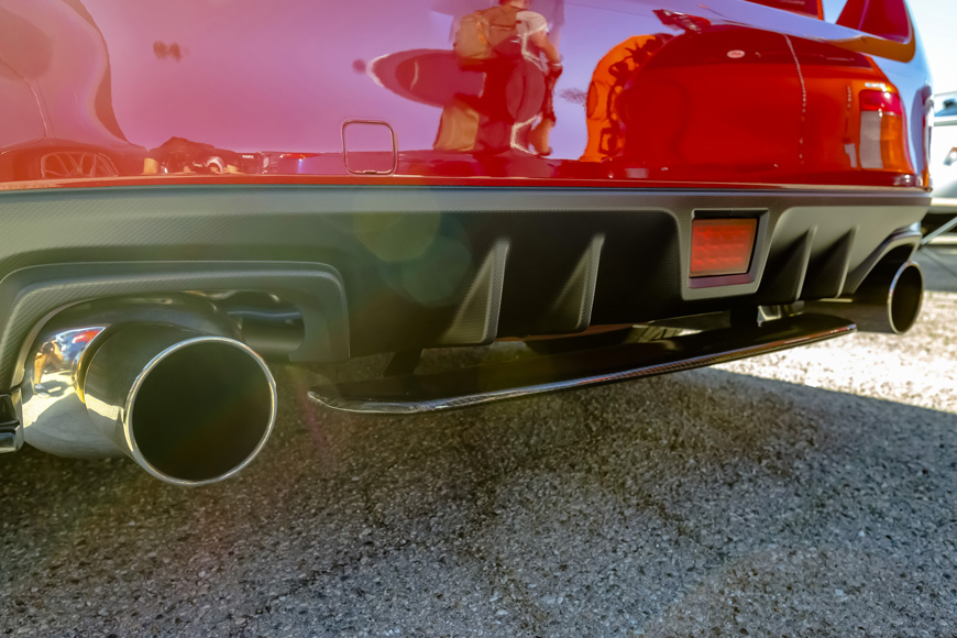 Shiny chrome exhaust pipes under a cherry red car