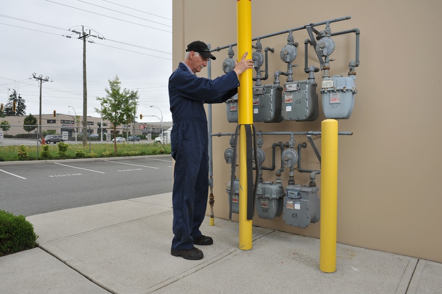A worker installing a plastic bollard in front of gas meters.