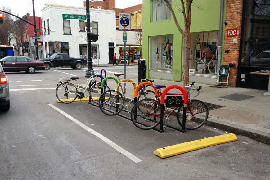 An on-street bike corral consists of five yarn-bombed U-racks in a rainbow of color