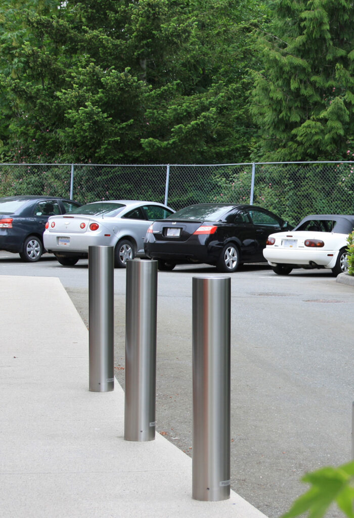 Three R-7303 stainless steel bollard covers with cars in the background