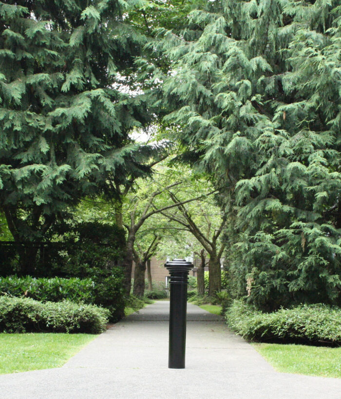 R-7573 decorative bollard on path in front of large trees and greenery