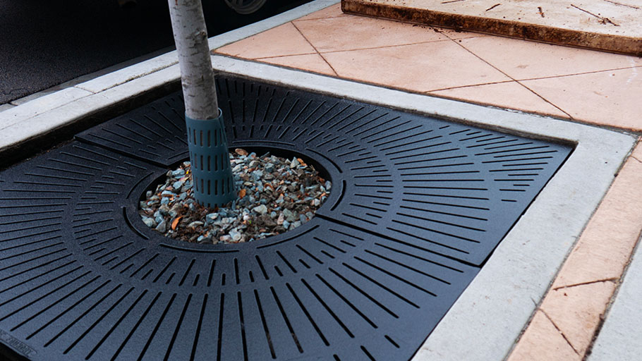 The Reliance Foundry R-8706 Metropolitan tree grate protects a tree in a plaza