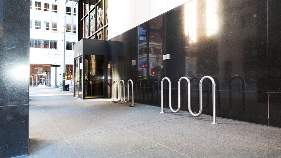 An image of two wave style bike racks installed in front of a modern building.
