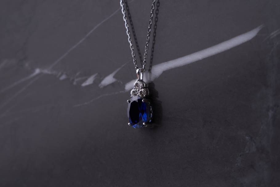 A sapphire gemstone hangs in a platinum setting on a platinum chain