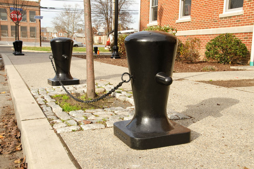 A black marine bollard with a wide top, tapering to a narrow base, features two rope-lashing arms
