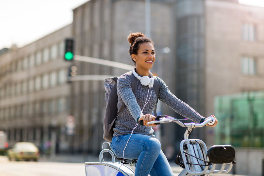 A young woman with a wide and engaging smile rides a bike-share bicycle on a city street