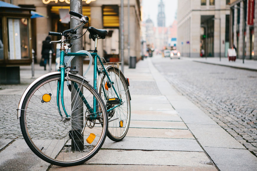 Teal bicycle locked to metal pole with a cable lock on a European street