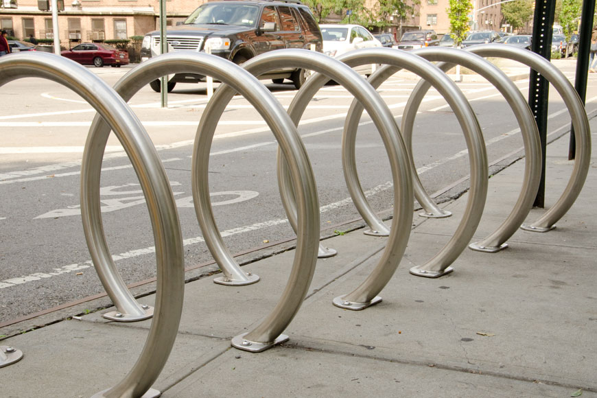 A set of circular bike racks sits on the curb of a busy street: blurred car behind.