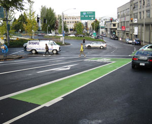 A green painted bike box sits before a busy intersection before a freeway onramp
