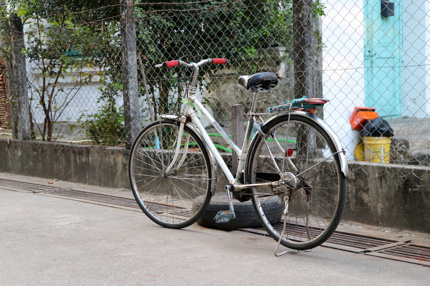 A bicycle stands by a car tire near a fence with a hazardous grate in front of it