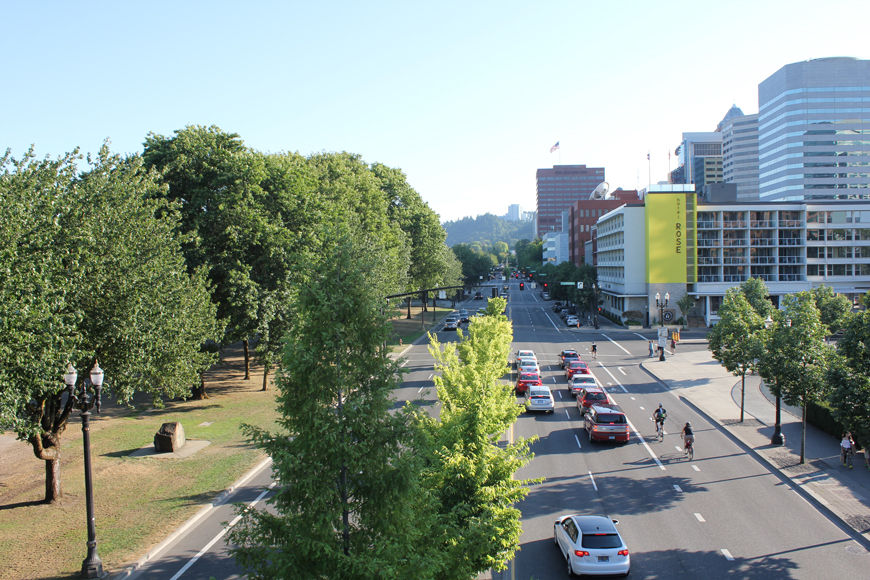 An aerial view of Naito St, Portland, shows a bike lane with riders, traffic, and a park