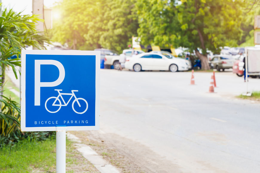 Blue bike parking sign stands in foreground, cars parked in background