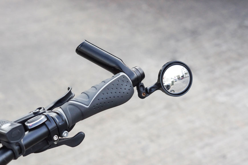 Close-up top-down image of handlebars with side mirror, road and cars reflected in surface