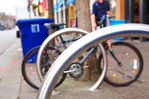 A series of curved stainless steel outdoor bike racks secure a brightly colored bicycle