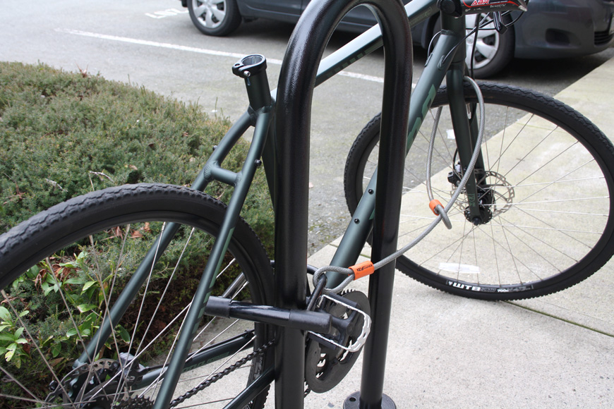 A green bicycle locked to a U-shaped outdoor bike rack is missing its seat