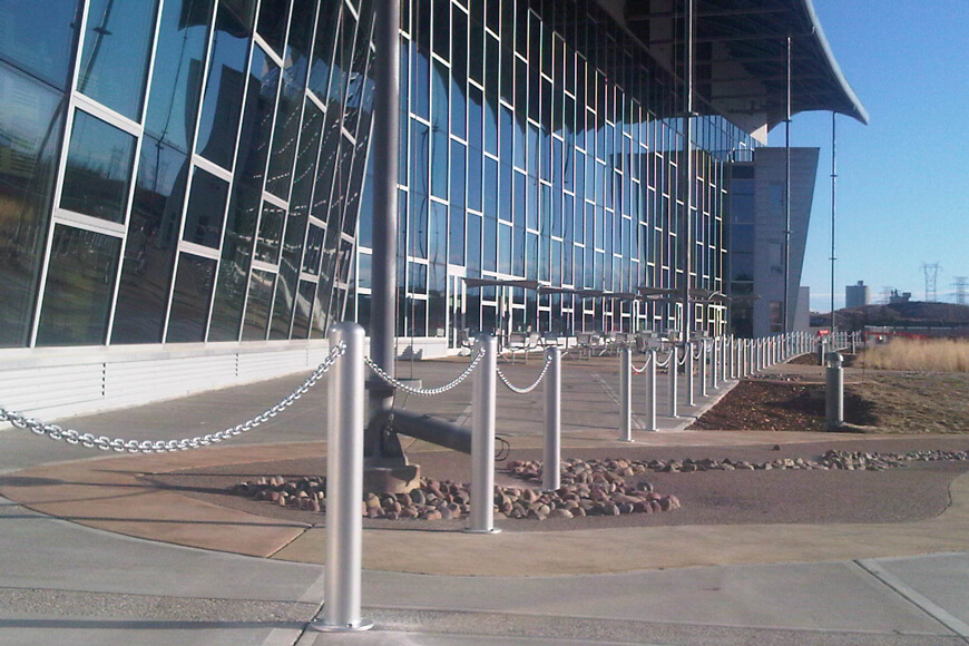 Several steel bollards are linked with a chain in front of a large modern building