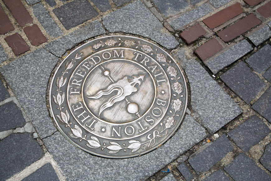 A bronze freedom trail medallion sunk into concrete points the direction of the freedom trail