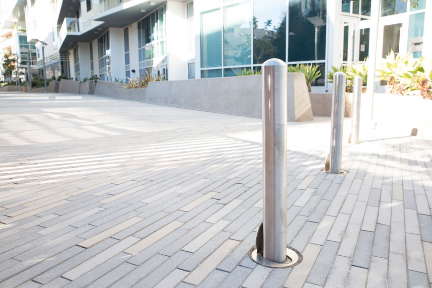 A stainless steel bollard stands on a sunny stone pathway