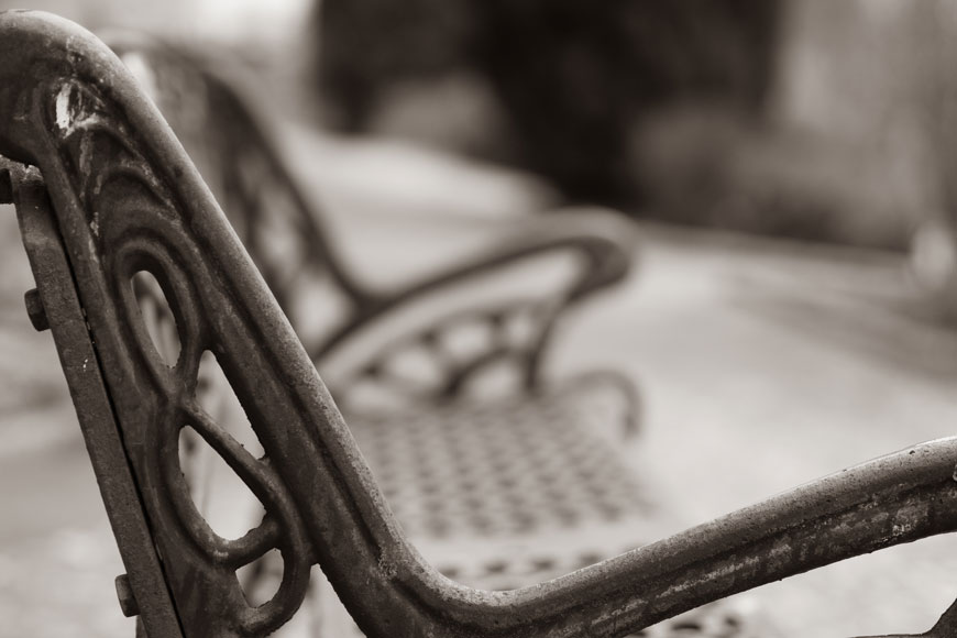 A close-up photograph of the ornate side of a weathered cast iron bench