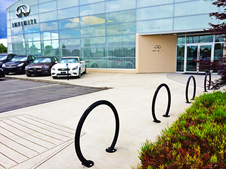 Four circular bike racks are placed in a line outside an Infiniti car dealership