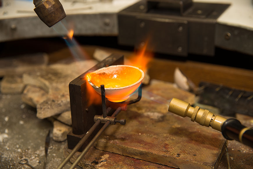 Two propane blowtorches heat a quarter cup sized crucible to melt precious metal. 