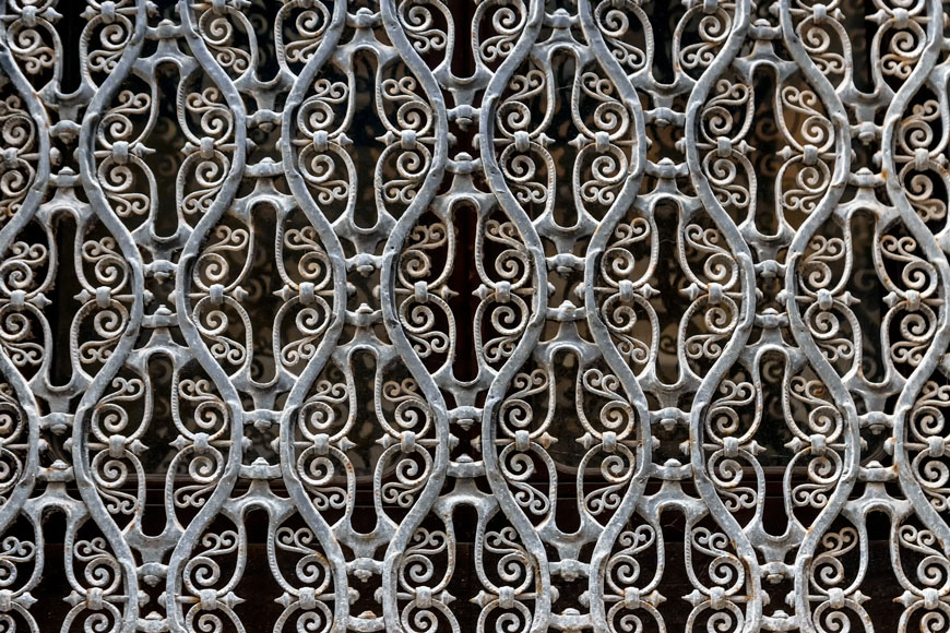 A lattice of white-painted aged gray iron creates a repeating fence pattern
