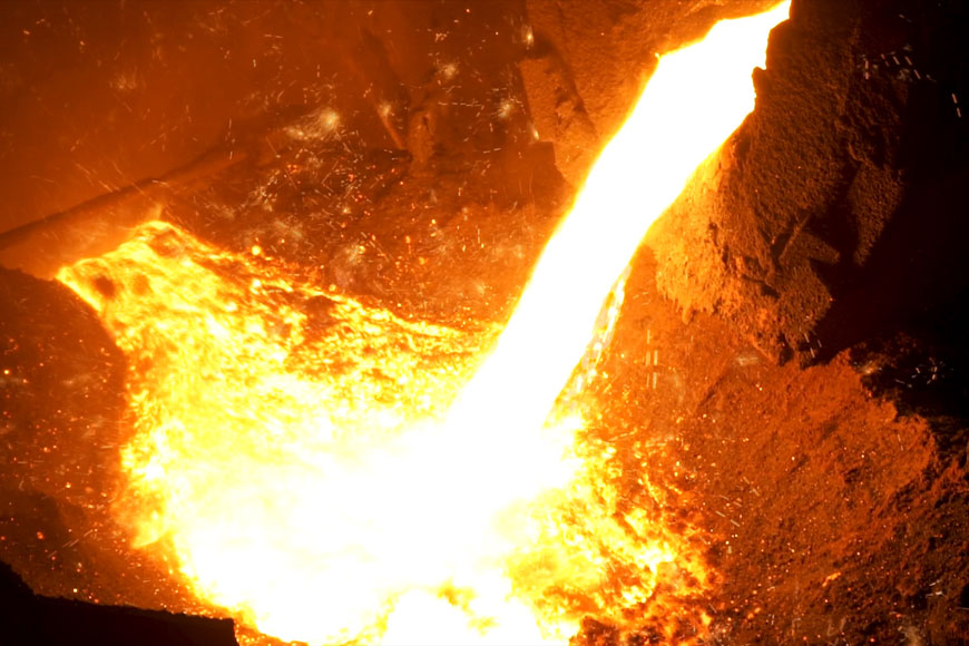 A glowing crucible of molten iron is being cast in a foundry