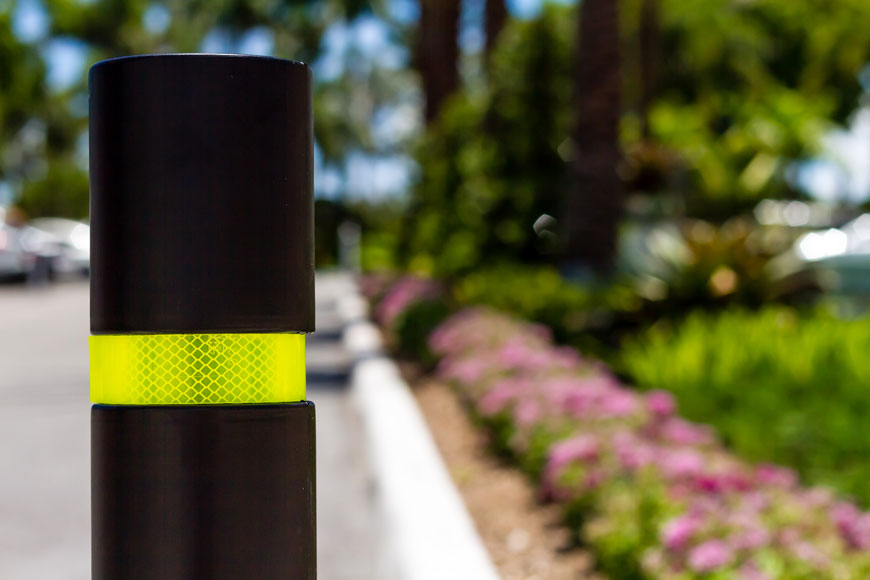 A black bollard with yellow reflective tape stands before a very blue sky