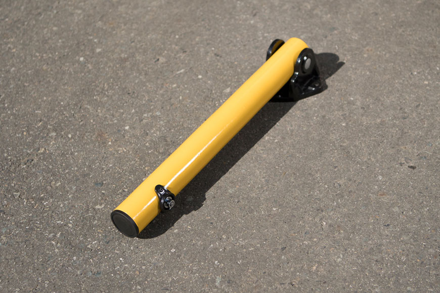 A yellow bollard is folded flat against the pavement of a parking space