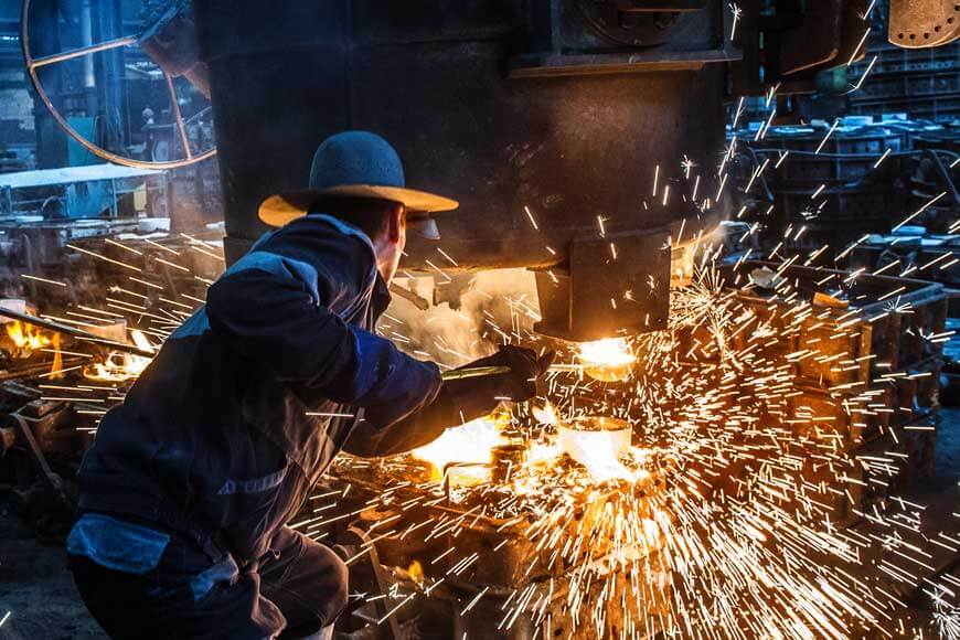 Foundry worker pouring molten metal into a sand mold using a bottom pour ladle