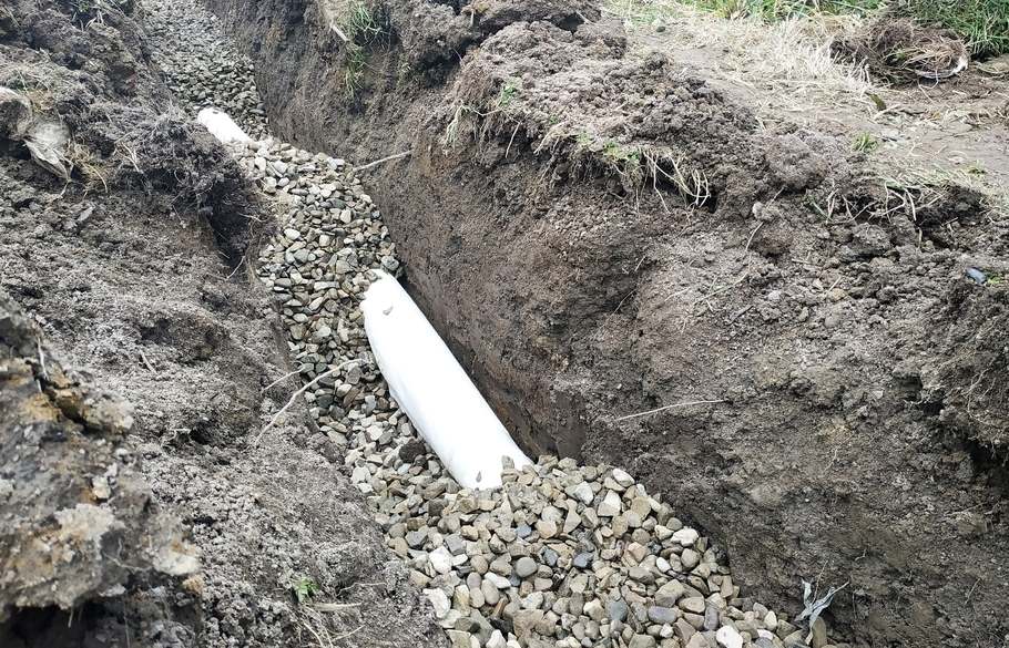A seam dug into the ground is being filled with pipe and gravel.