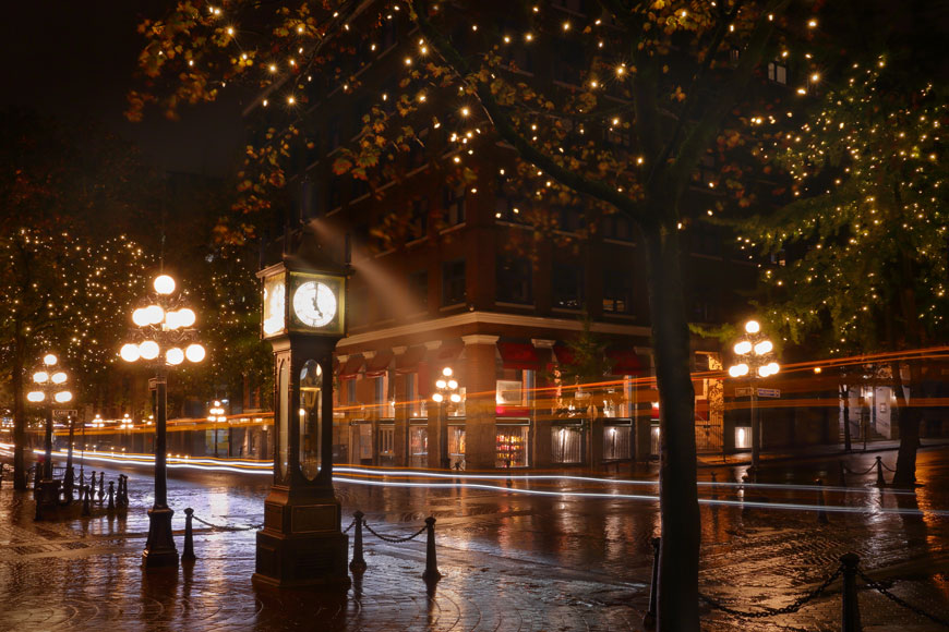 On a dark night in a historical downtown, the lights of ball lamps and a steam clock cast a golden glow.