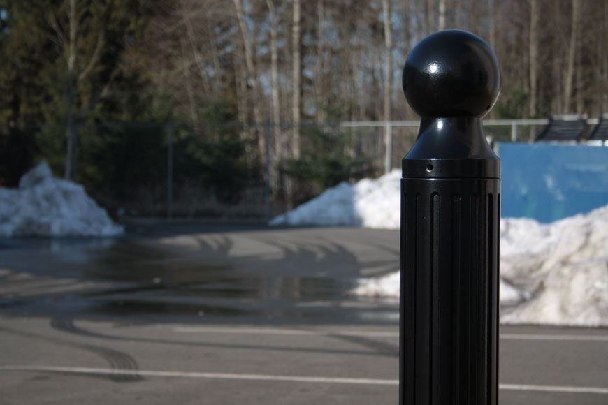A black bollard stands in a parking lot filled with mounded snow