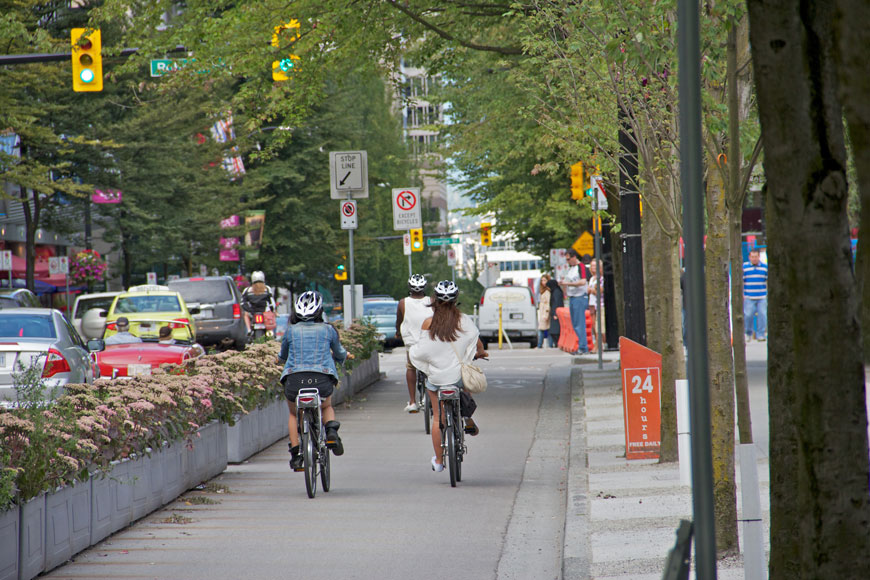 Three cyclists zip down a bike lane separated from traffic by planters filled with flowers