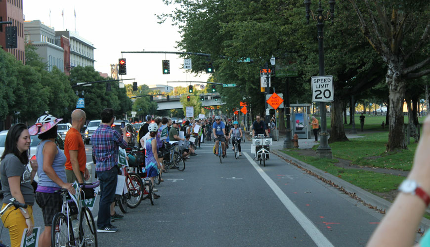 A line of people as “human bollards” stand between a cycle lane and traffic and cheer riders on