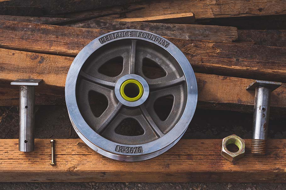 A shiny steel wheel with a green Nyloil bushing sits on several pieces of wood with attachment hardware nearby