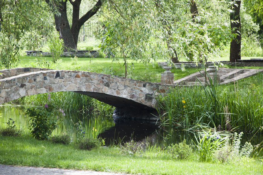 A bucolic landscape of a stone bridge over a body of water surrounded by willows