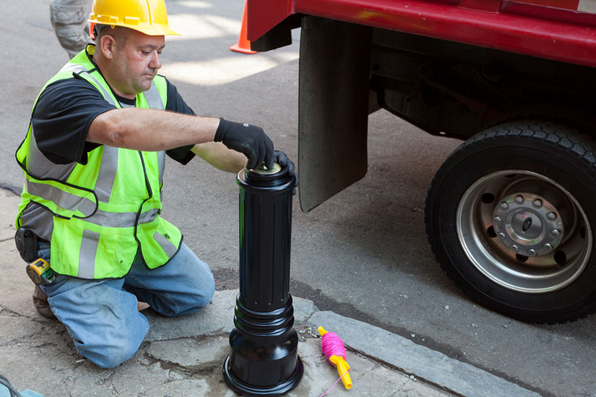 A worker tightens a nut on a 1" threaded rod to secure the body of a decorative bollard.