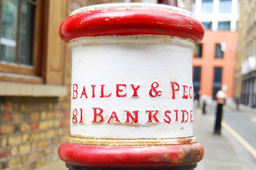 An old cannon bollard painted black, white and red is embossed Bailey & Pegg, 81 Bankside