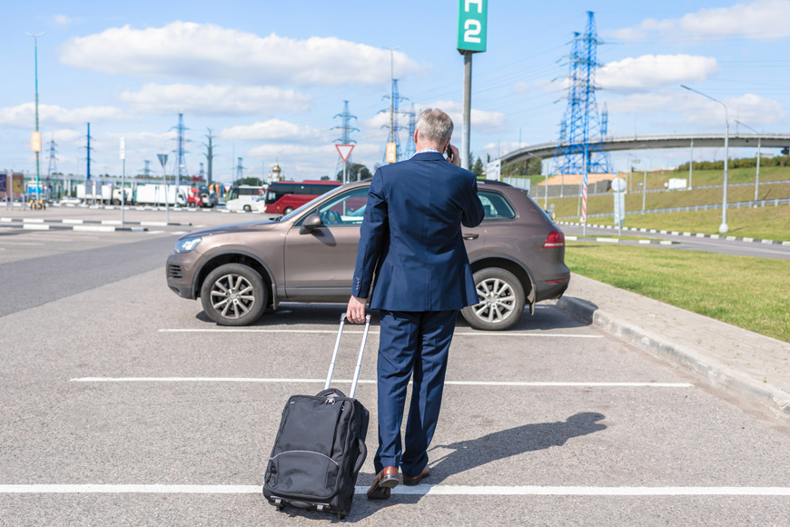 A businessman walks with a wheeled carry-on to his car in a long term lot