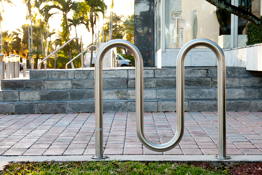 A silver wave bike rack sits beside stone steps in front of a sleek marble and glass storefront