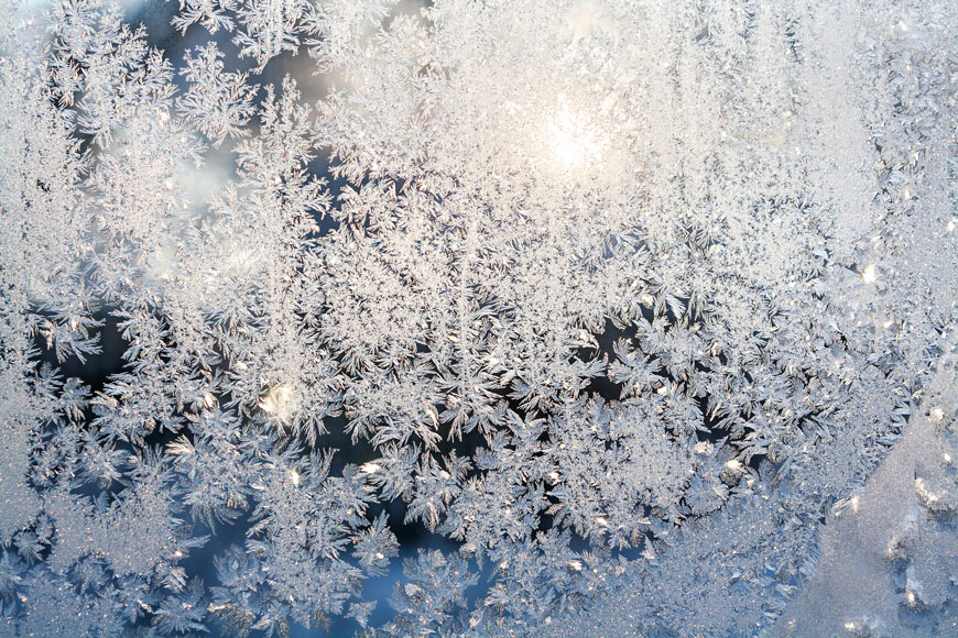 Sun shines through a window covered in wintery blooms of frost