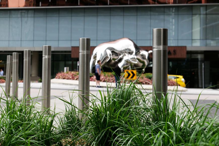 A series of bollards beside grass with silver finance bull statue behind