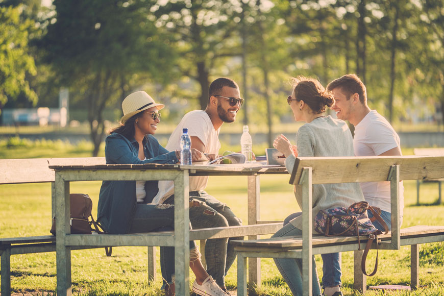 A group of friends sit together at a large picnic table in a park