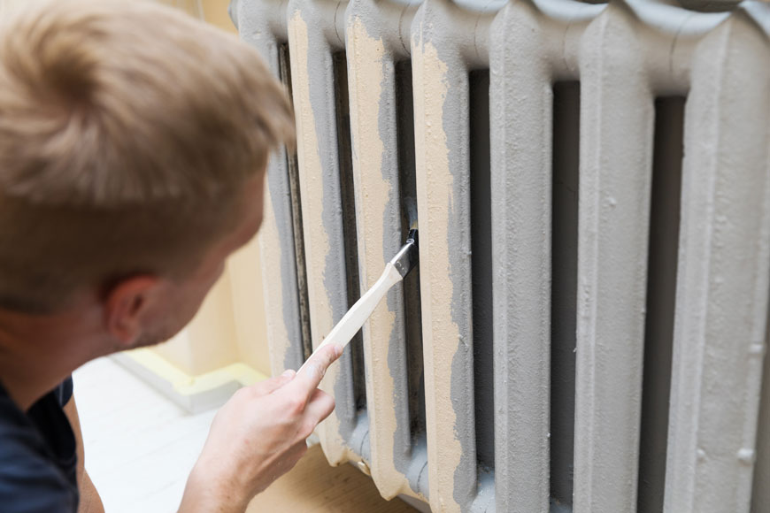 A worker paints a metal steam-radiator with a small paintbrush
