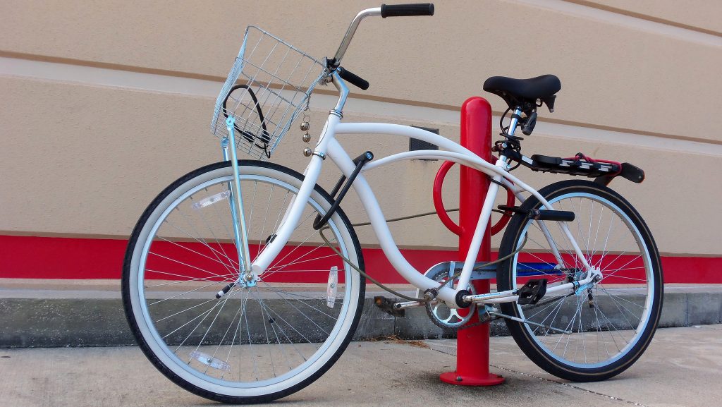 a white bicycle is locked to a bike bollard with a cable lock