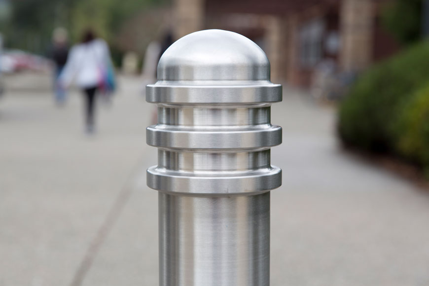 A stainless steel bollard in front of an outdoor walkway